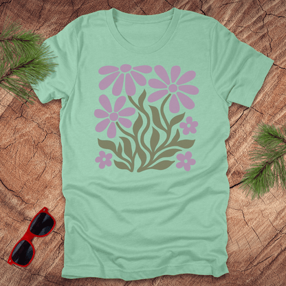 Light green t-shirt with pink floral design on a wooden surface with sunglasses and greenery.