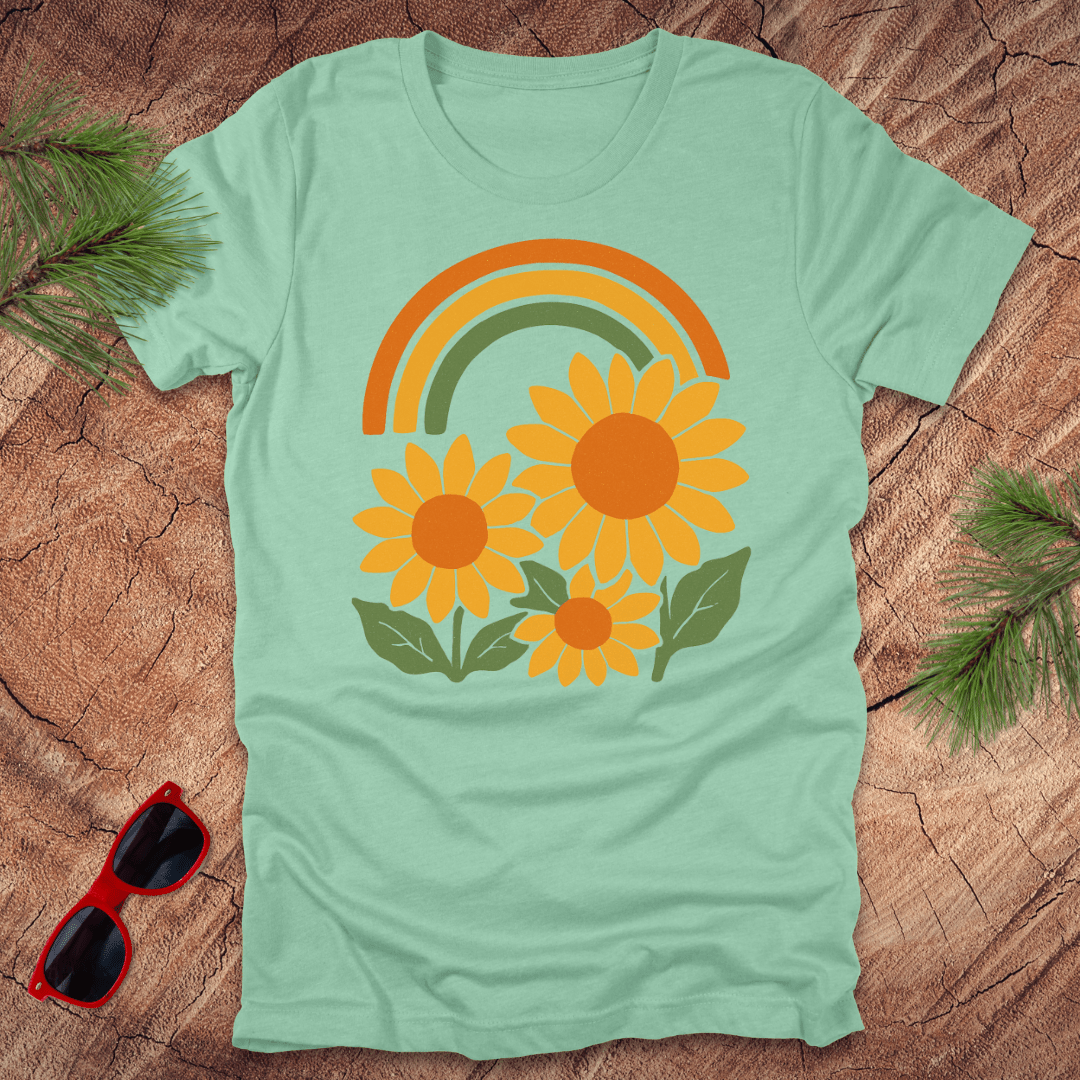 mint green t-shirt with sunflower and rainbow design on a wooden surface with sunglasses and leaves.
