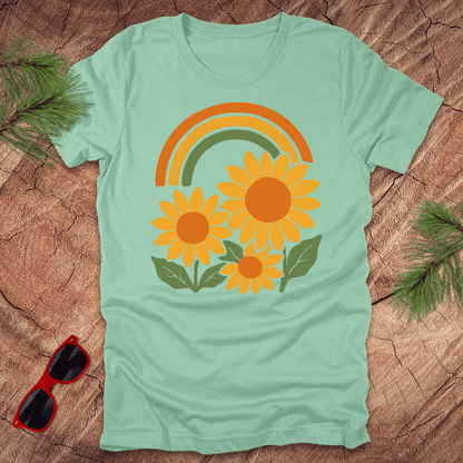 mint green t-shirt with sunflower and rainbow design on a wooden surface with sunglasses and leaves.
