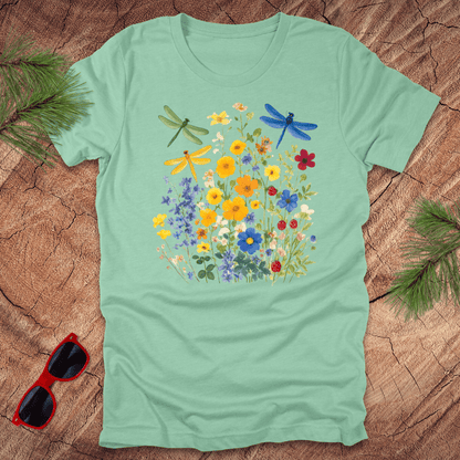 Light green t-shirt with floral and dragonfly design on a wooden surface with sunglasses and foliage.