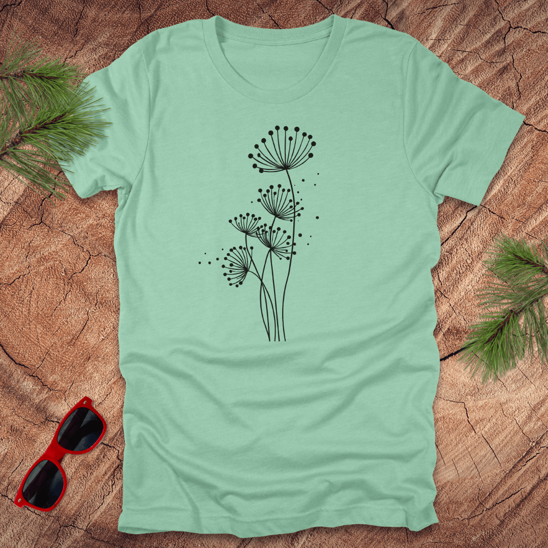 Light blue t-shirt with black floral dandelion design on a wooden surface with sunglasses and greenery.
