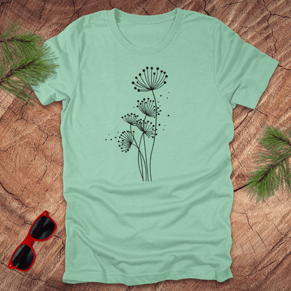 Light blue t-shirt with black floral dandelion design on a wooden surface with sunglasses and greenery.