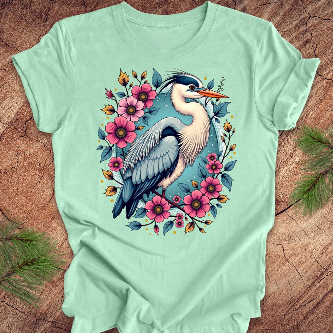 Mint green t-shirt with a heron and floral design on a wood background.