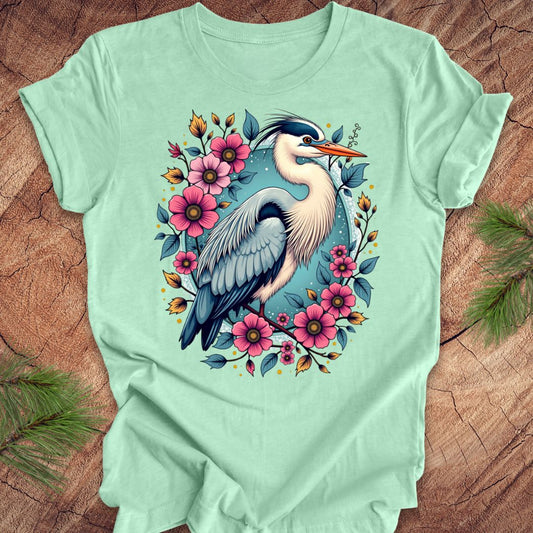 Mint green t-shirt with a heron and floral design on a wood background.