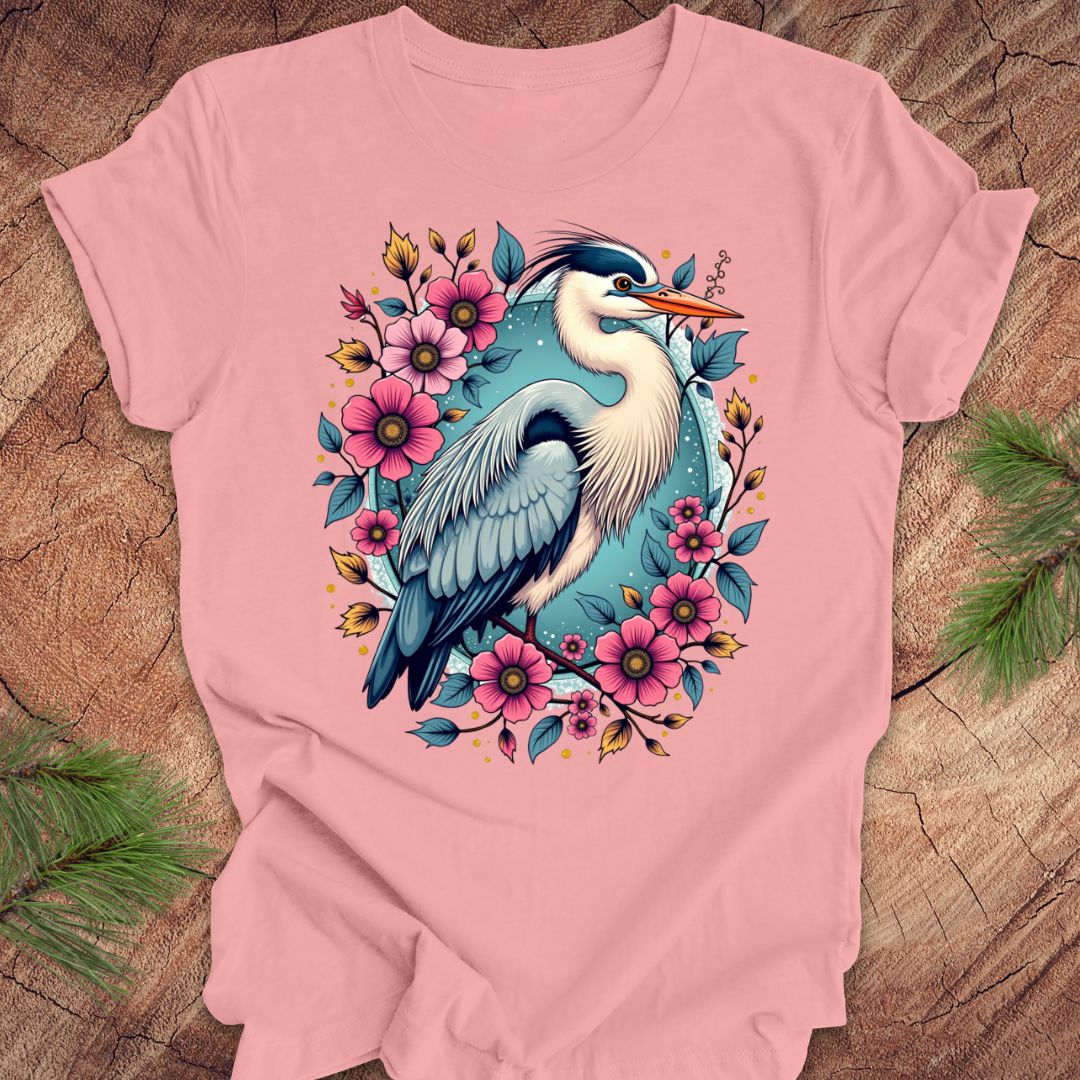 Pink t-shirt with a heron and floral design on a wood background.