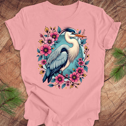 Pink t-shirt with a heron and floral design on a wood background.