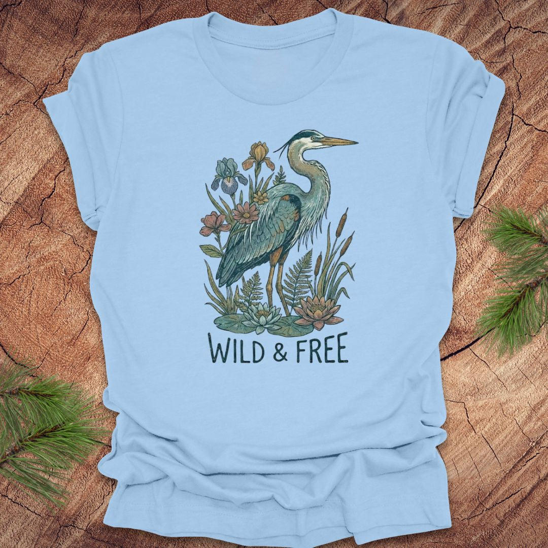 Baby blue t-shirt with a heron and floral design with text, 'wild and free' on a wooden surface
