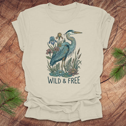 Beige t-shirt with a heron and floral design with text, 'wild and free' on a wooden surface