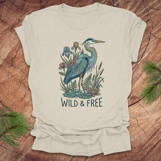 Beige t-shirt with a heron and floral design with text, 'wild and free' on a wooden surface