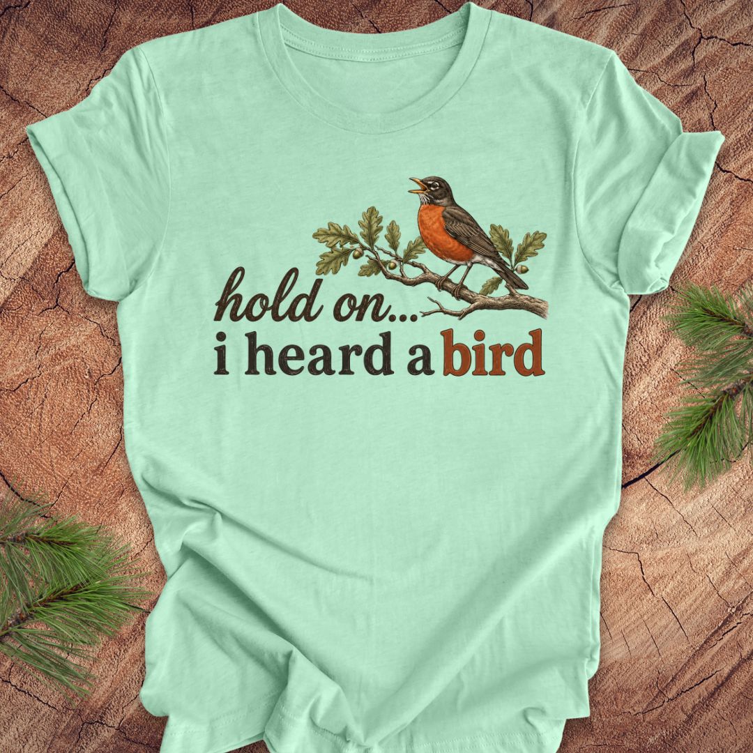 Light green t-shirt with a bird graphic and text on a wooden surface