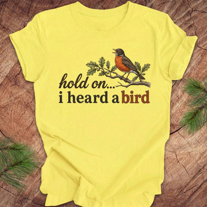 Yellow t-shirt with a bird graphic and text on a wooden surface