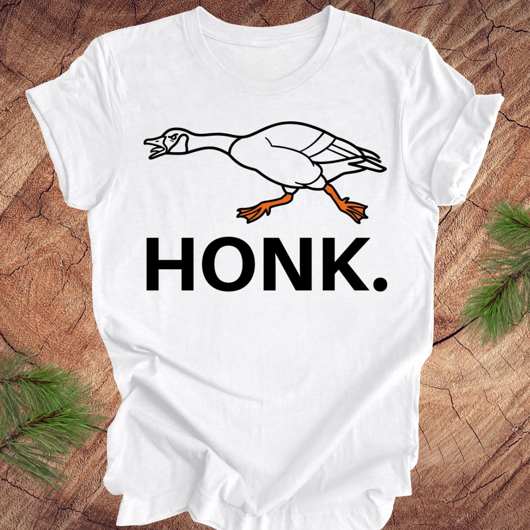 White t-shirt with a goose graphic and 'HONK.' text on a wooden surface.
