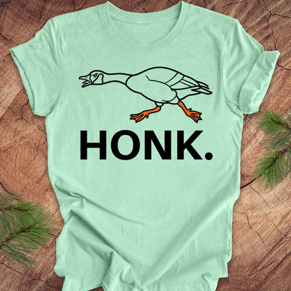 Mint green t-shirt with a goose graphic and 'HONK.' text on a wooden surface.