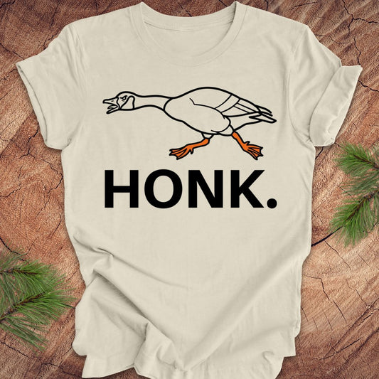 Beige t-shirt with a goose graphic and 'HONK.' text on a wooden surface.
