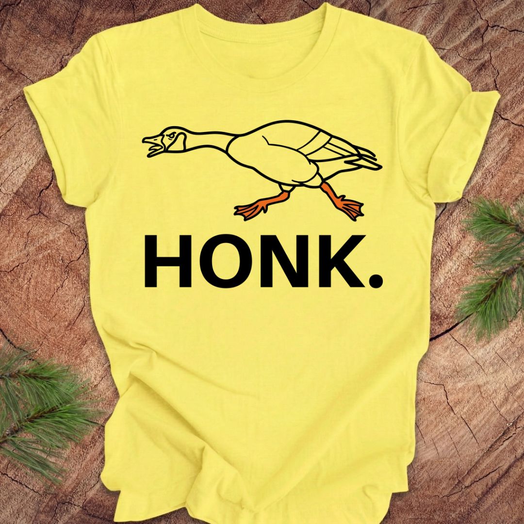 Yellow t-shirt with a goose graphic and 'HONK.' text on a wooden surface.