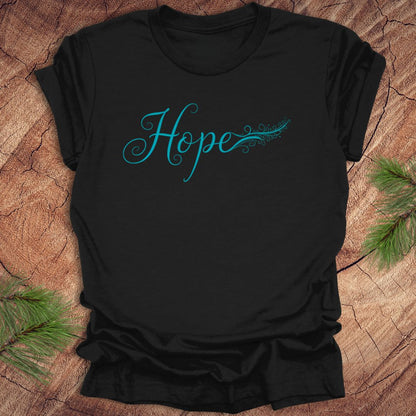 Black t-shirt with hand drawn text, 'Hope' in turquoise on a wooden surface with greenery.