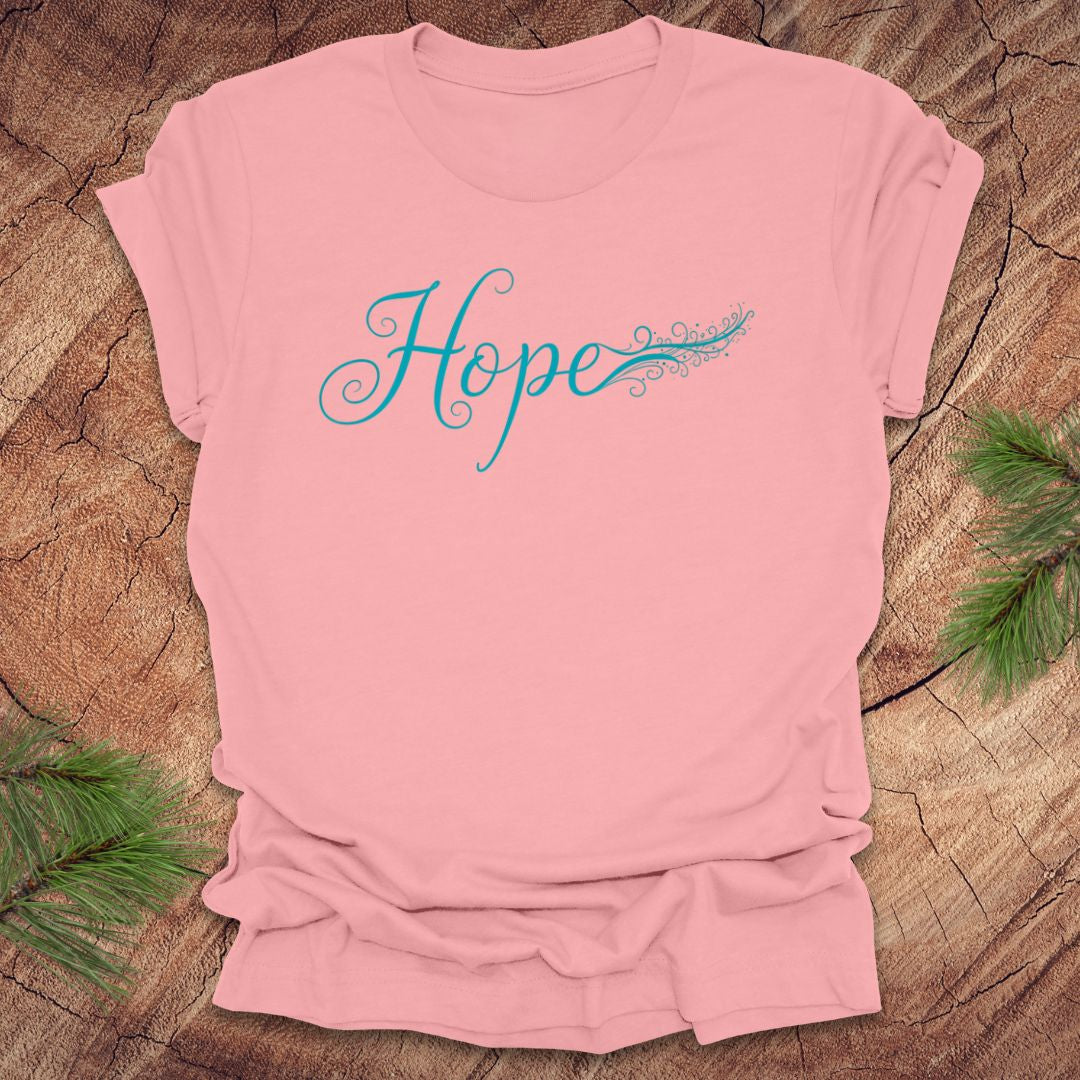 Pink t-shirt with hand drawn text, 'Hope' in turquoise on a wooden surface with greenery.