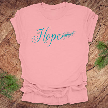 Pink t-shirt with hand drawn text, 'Hope' in turquoise on a wooden surface with greenery.