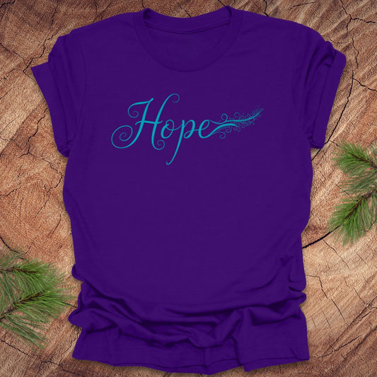 Purple t-shirt with hand drawn text, 'Hope' in turquoise on a wooden surface with greenery.