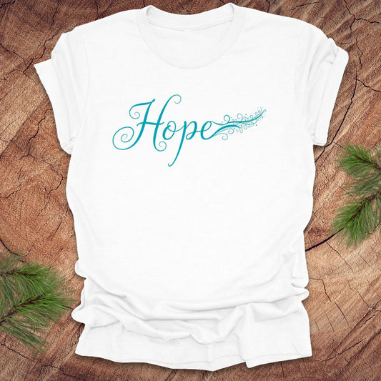 White t-shirt with hand drawn text, 'Hope' in turquoise on a wooden surface with greenery.