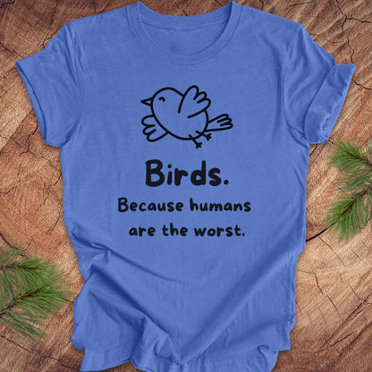 Blue t-shirt with a bird and text, 'birds. because humans are the worst.' on a wood background. 