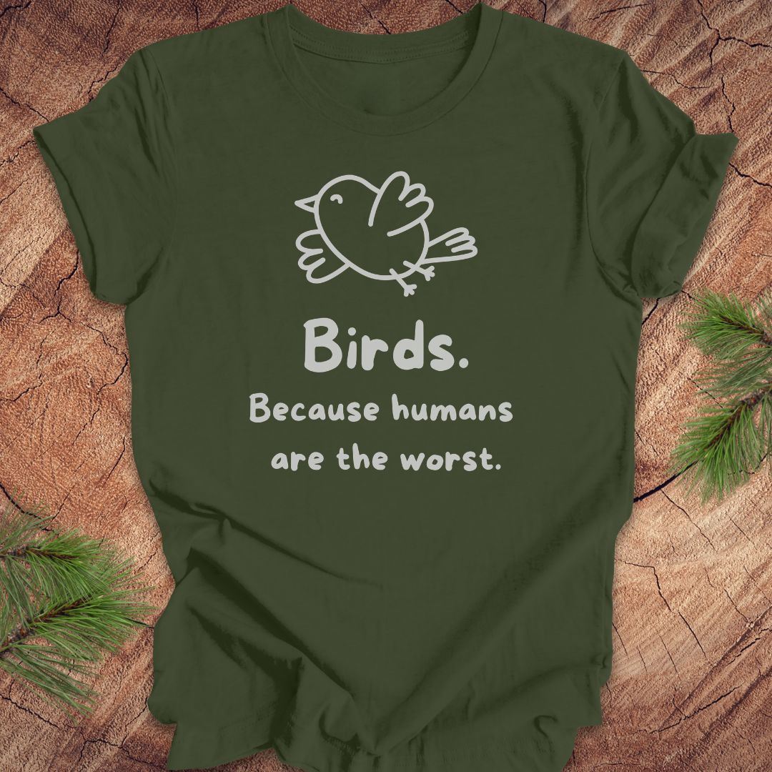 Green t-shirt with a bird and text, 'birds. because humans are the worst.' on a wood background. 