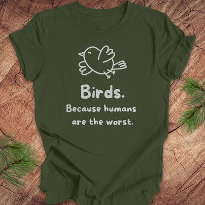 Green t-shirt with a bird and text, 'birds. because humans are the worst.' on a wood background. 