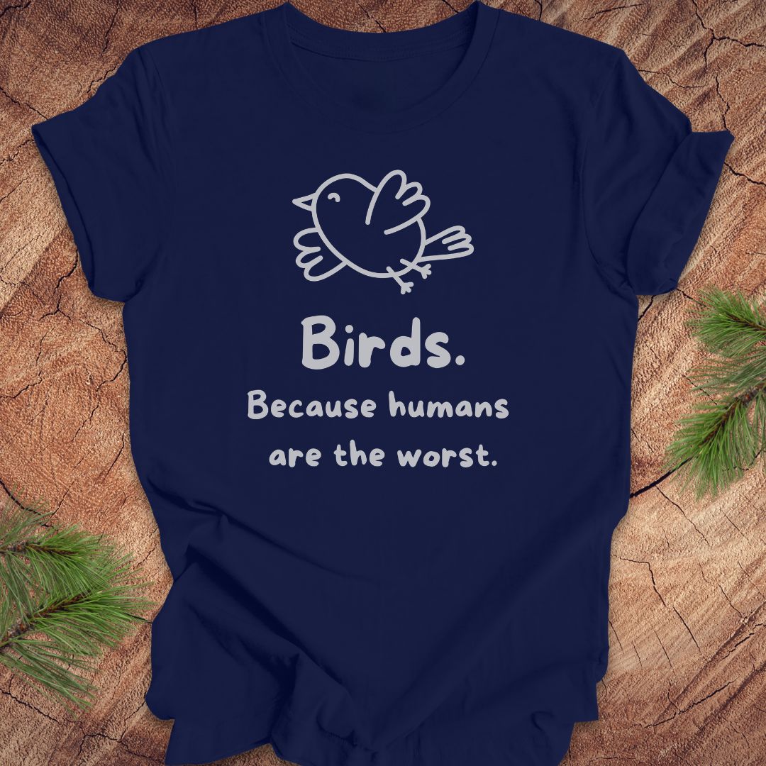 Navy blue t-shirt with a bird and text, 'birds. because humans are the worst.' on a wood background. 