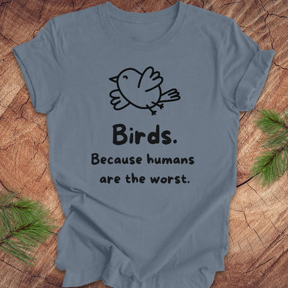 Blue t-shirt with a bird and text, 'birds. because humans are the worst.' on a wood background. 