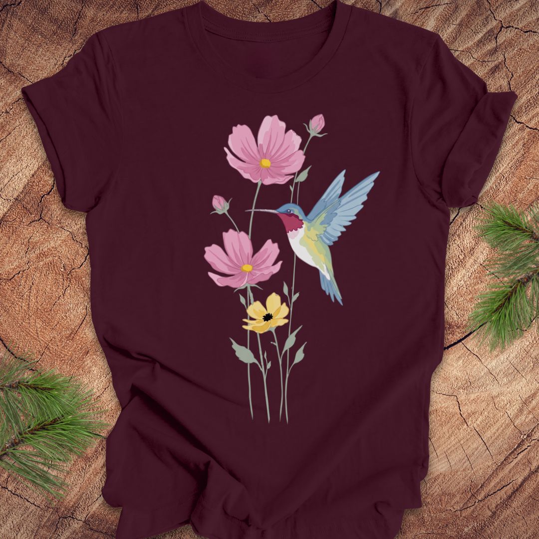 Maroon t-shirt with a colorful hummingbird and flower design on a wooden surface.