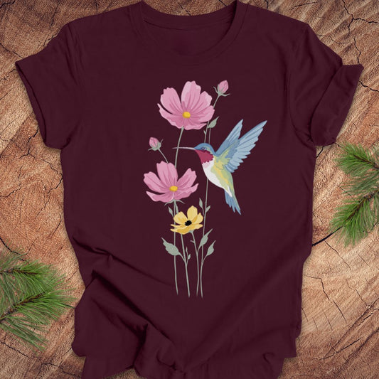 Maroon t-shirt with a colorful hummingbird and flower design on a wooden surface.