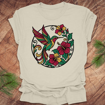 Beige t-shirt with a colorful hummingbird and floral design on a wooden surface.