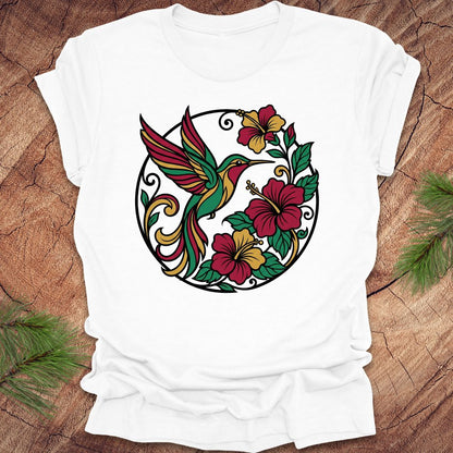 White t-shirt with a colorful hummingbird and floral design on a wooden surface.