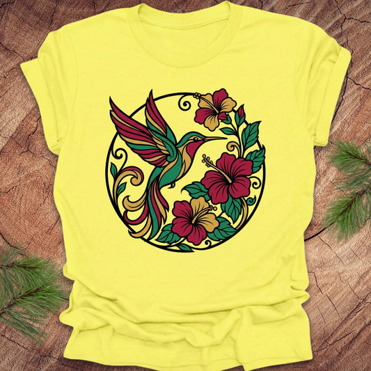 Yellow t-shirt with a colorful hummingbird and floral design on a wooden surface.