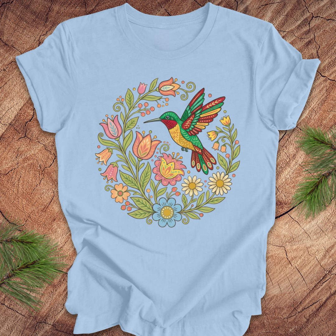 Light blue t-shirt with a colorful hummingbird and floral design on a wooden surface.