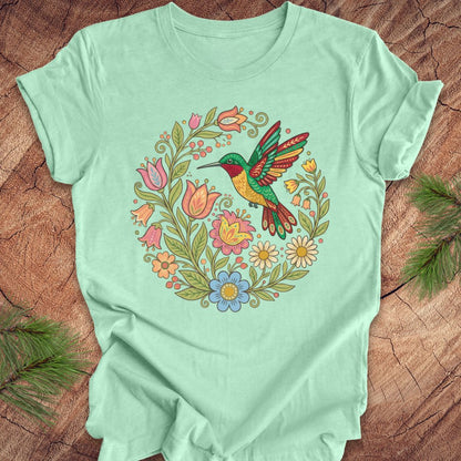 Mint green t-shirt with a colorful hummingbird and floral design on a wooden surface.