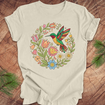 Beige t-shirt with a colorful hummingbird and floral design on a wooden surface.