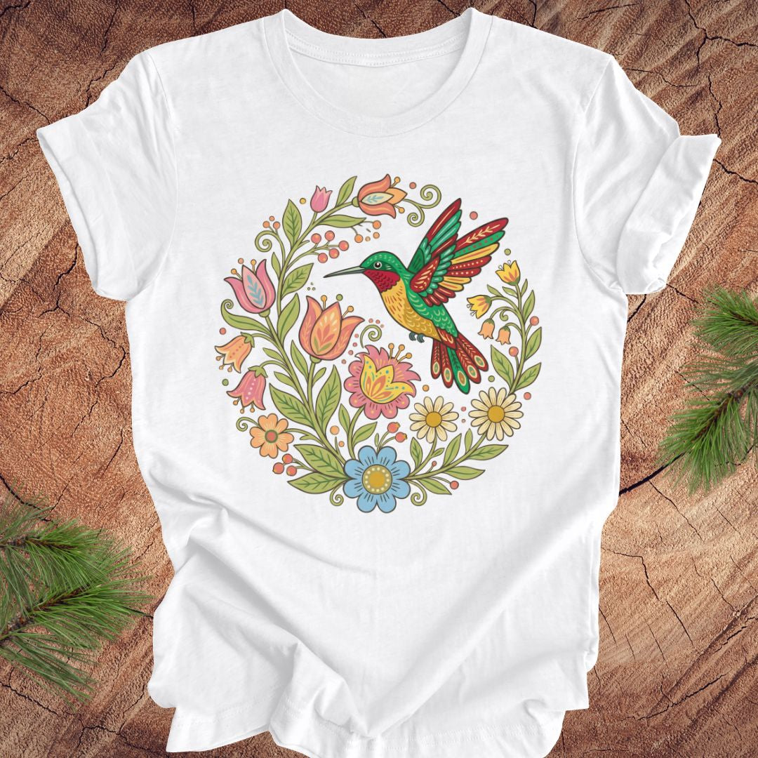 White t-shirt with a colorful hummingbird and floral design on a wooden surface.