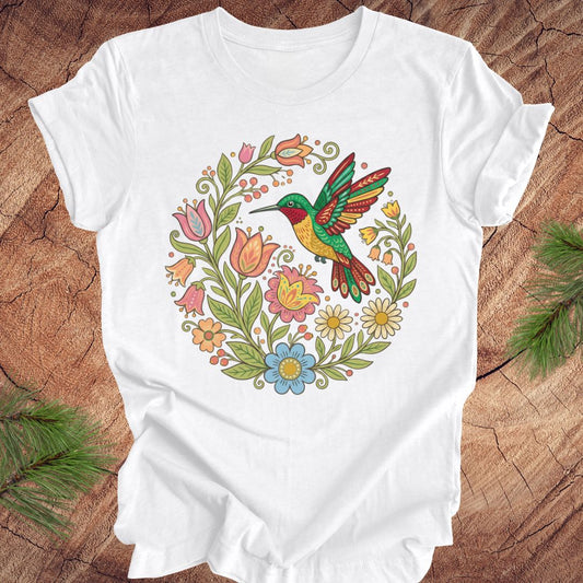 White t-shirt with a colorful hummingbird and floral design on a wooden surface.