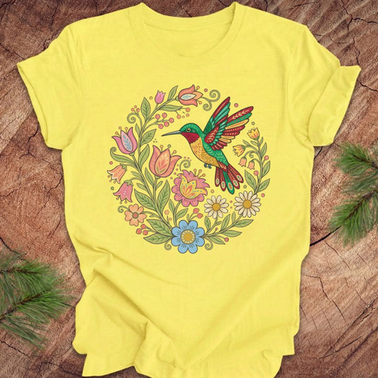 Yellow t-shirt with a colorful hummingbird and floral design on a wooden surface.