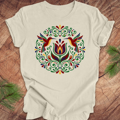 Beige t-shirt with colorful floral design and hummingbirds on a wooden surface