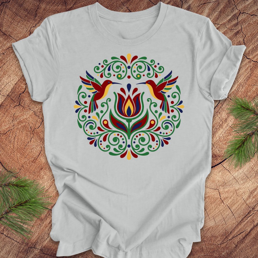Gray t-shirt with colorful floral design and hummingbirds on a wooden surface
