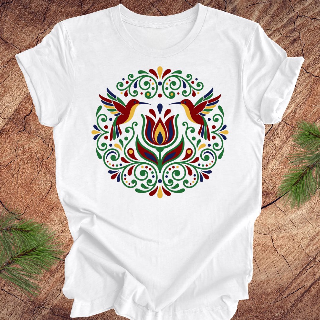 White t-shirt with colorful floral design and hummingbirds on a wooden surface
