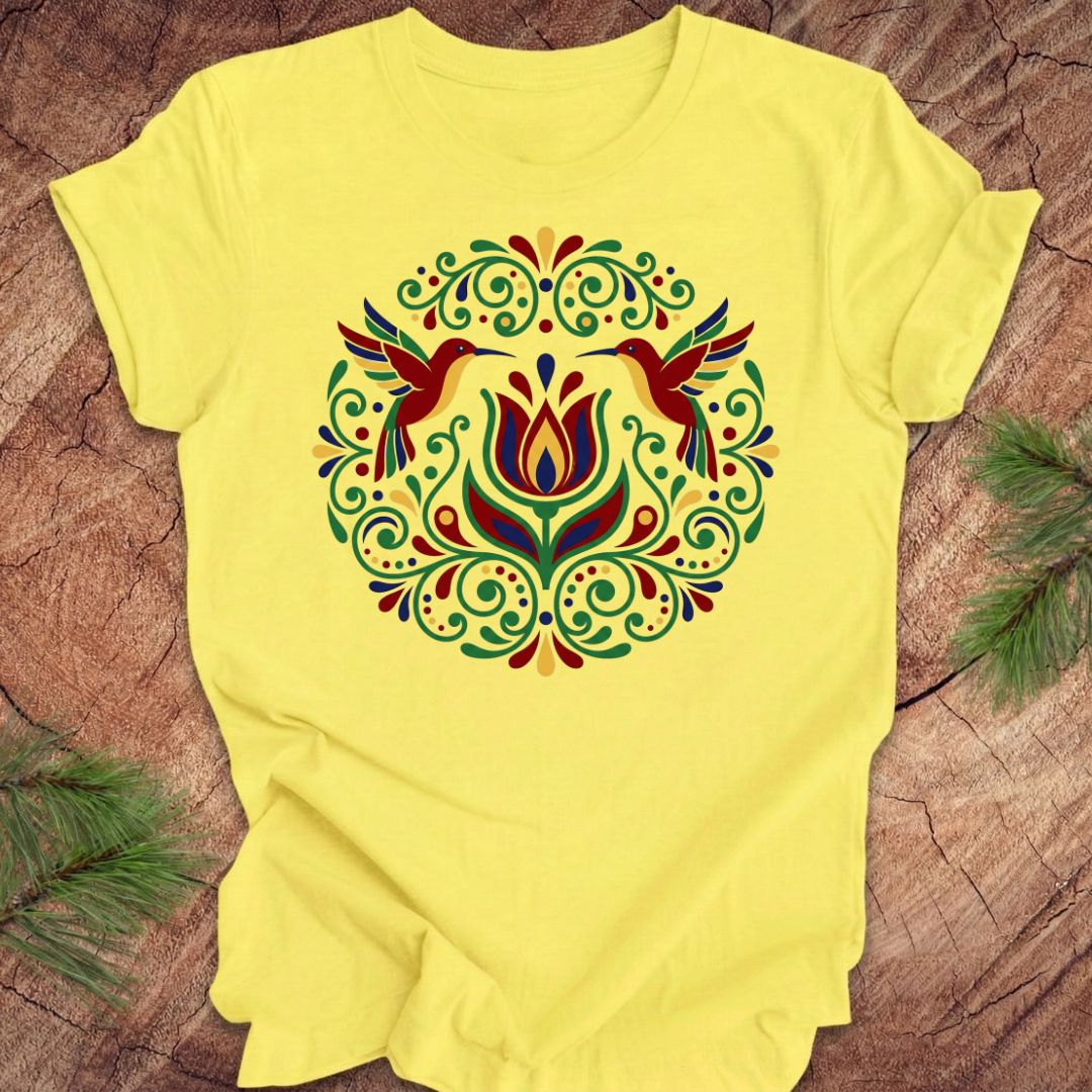 Yellow t-shirt with colorful floral design and hummingbirds on a wooden surface