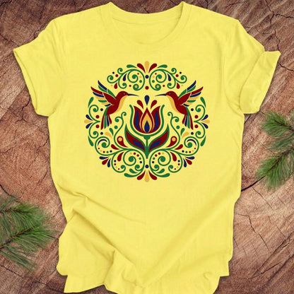 Yellow t-shirt with colorful floral design and hummingbirds on a wooden surface