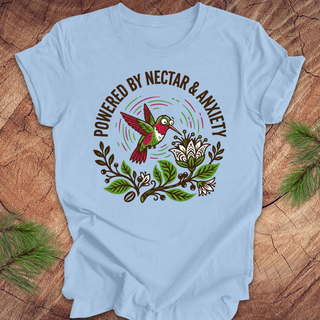 Light blue t-shirt with a colorful hummingbird graphic and text 'Powered by Nectar & Anxiety' on a wooden surface.