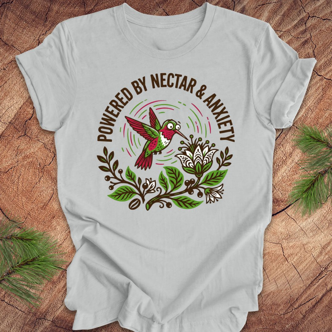 Gray t-shirt with a colorful hummingbird graphic and text 'Powered by Nectar & Anxiety' on a wooden surface.