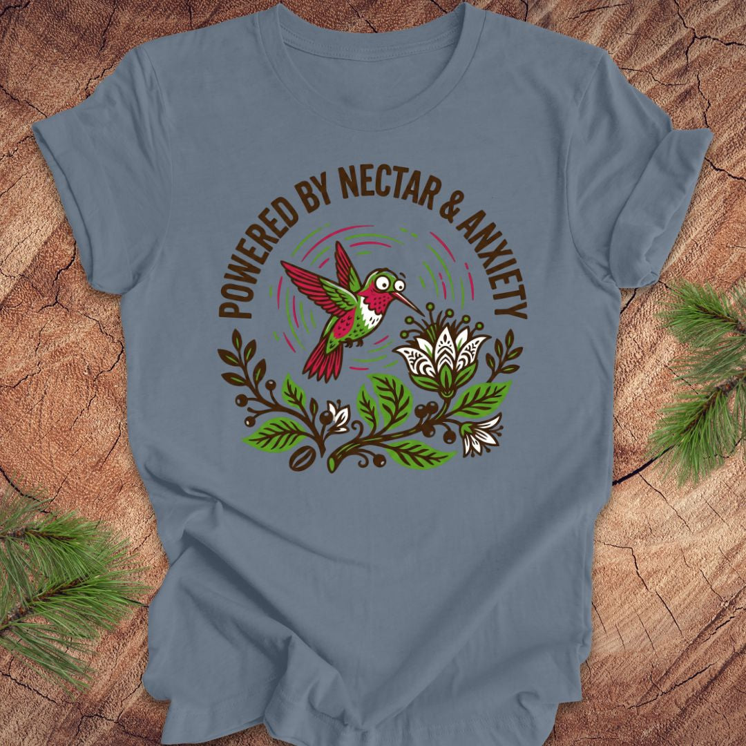 Steel blue t-shirt with a colorful hummingbird graphic and text 'Powered by Nectar & Anxiety' on a wooden surface.