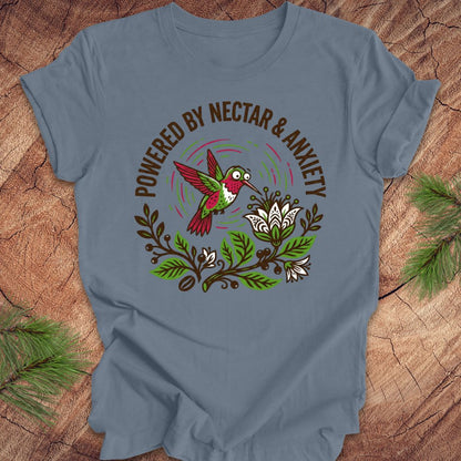 Steel blue t-shirt with a colorful hummingbird graphic and text 'Powered by Nectar & Anxiety' on a wooden surface.
