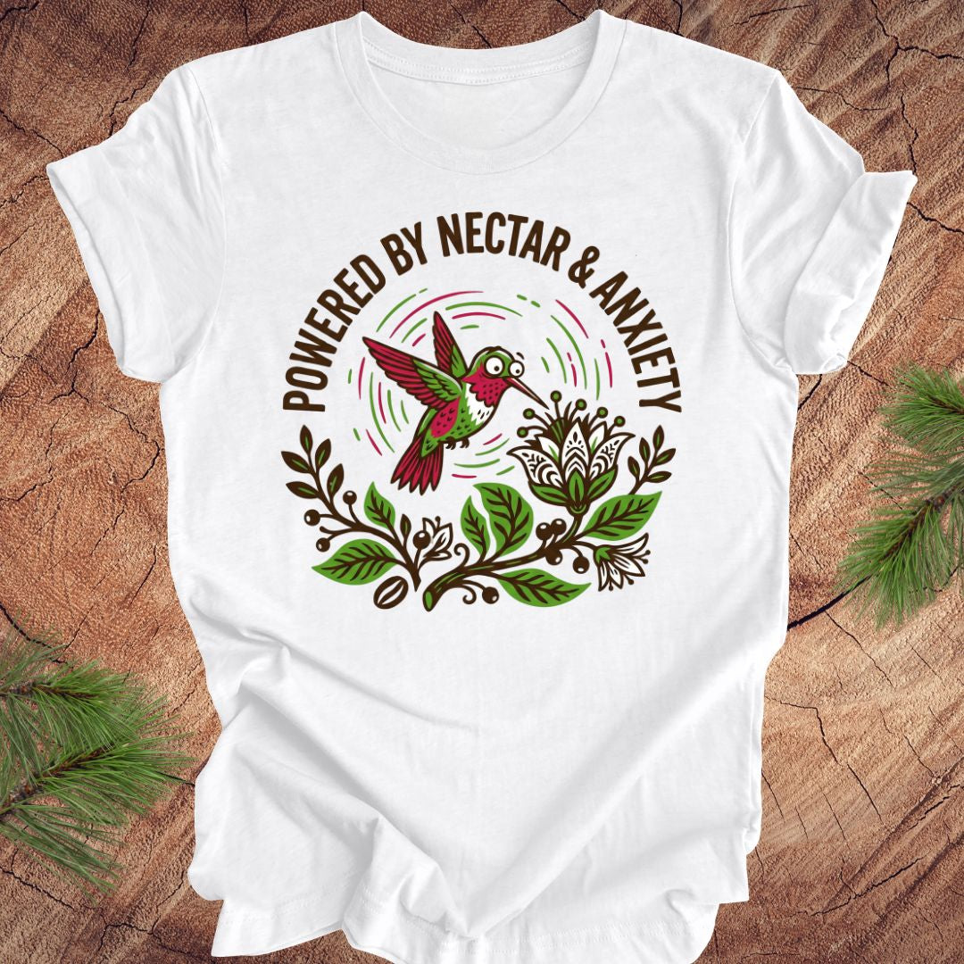 White t-shirt with a colorful hummingbird graphic and text 'Powered by Nectar & Anxiety' on a wooden surface.